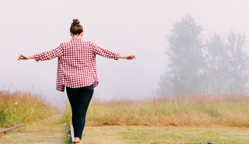 A woman is standing on a train track with her arms outstretched.
