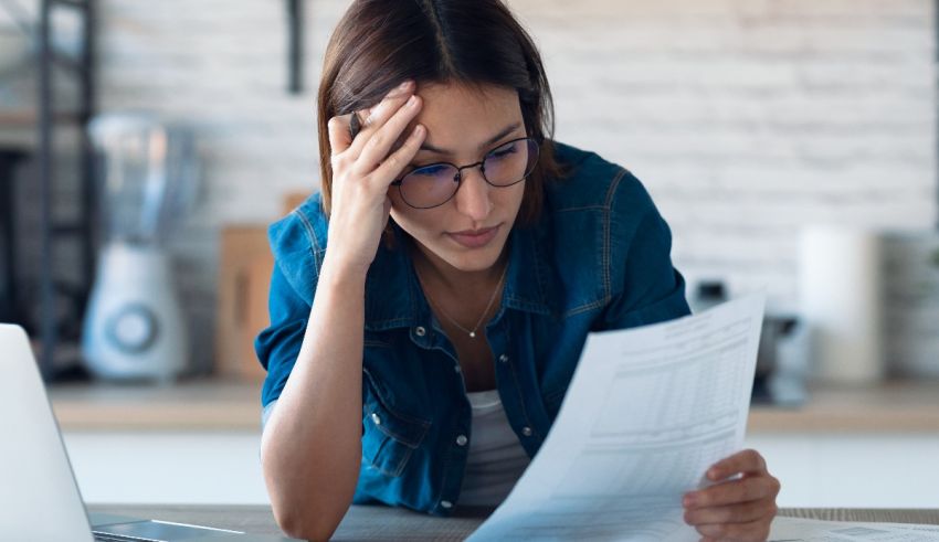A woman is sitting at a desk with papers and a laptop.