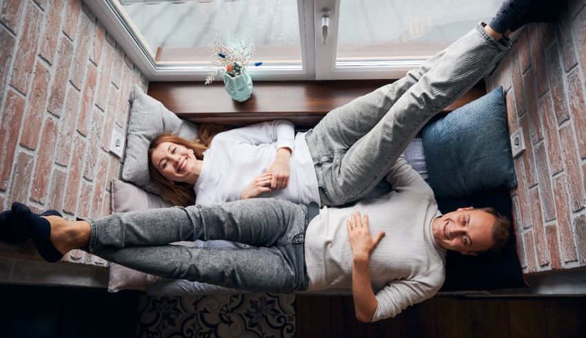 A man and woman are laying on a bed in a room with a window.
