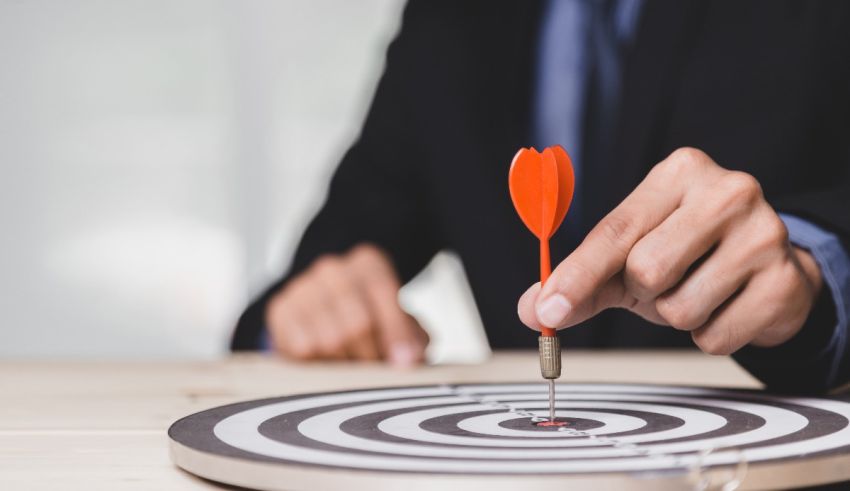 A businessman in a suit is aiming a dart at a target.