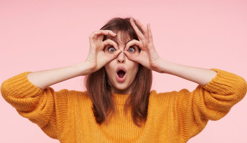 A young woman covering her eyes with her hands on a pink background.