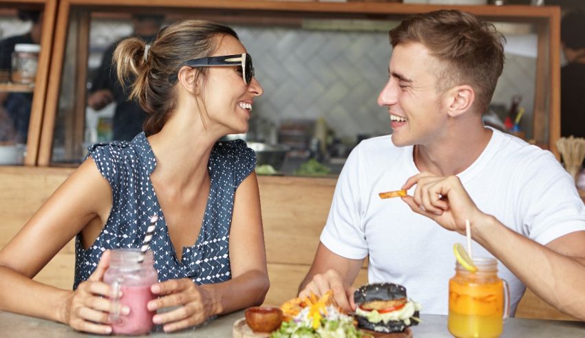 A man and woman are sitting at a table with food and drinks.