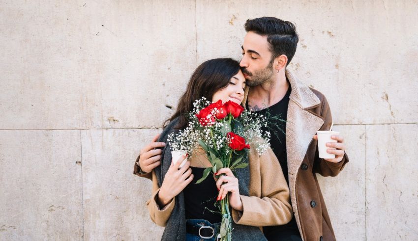 A man and woman hugging and kissing in front of a wall.