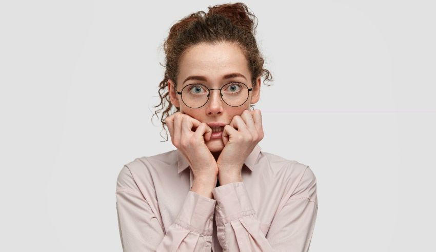 A woman with glasses covering her face with her hands.