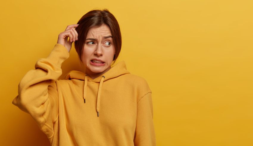 A woman in a yellow sweatshirt with her hand on her head.