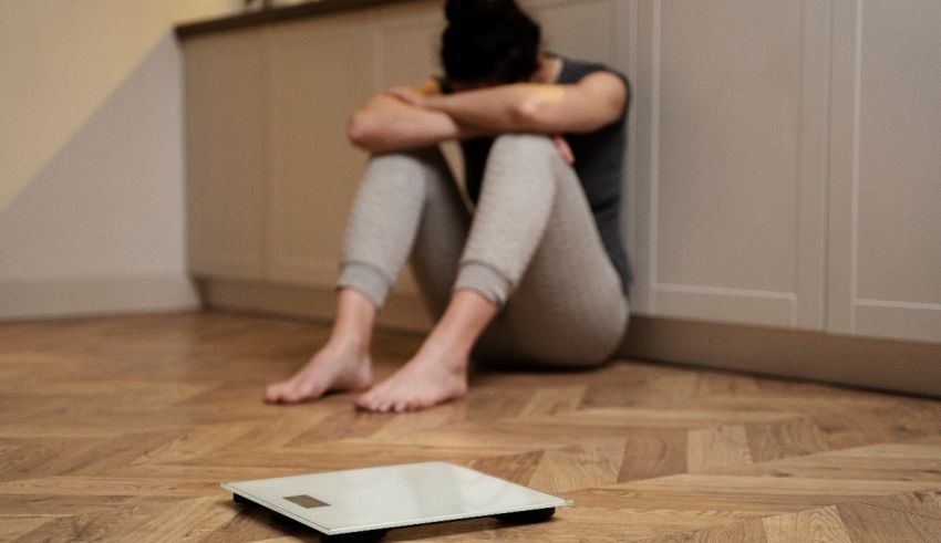 A woman sitting on the floor next to a scale.