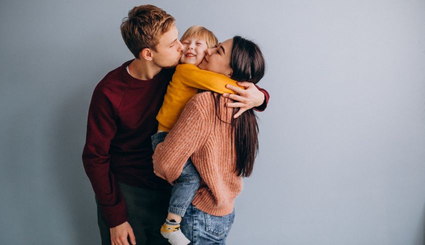 A family hugging and kissing their child on a gray background.