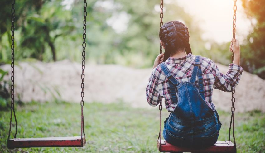 A girl sitting on a swing in a park.