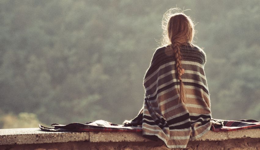 A woman sitting on a ledge with a blanket over her head.