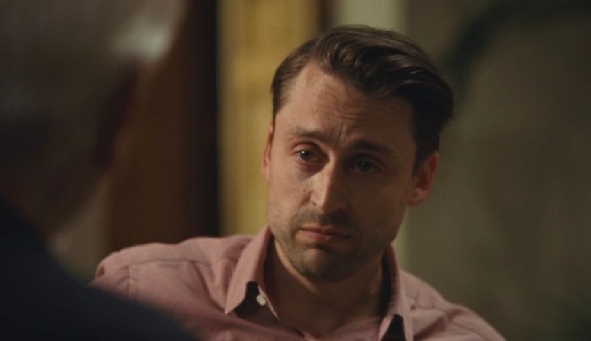 A man in a pink shirt is talking to an older man.