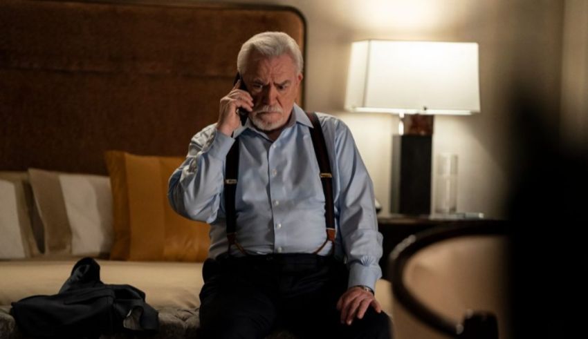 An older man sitting on a bed talking on a cell phone.