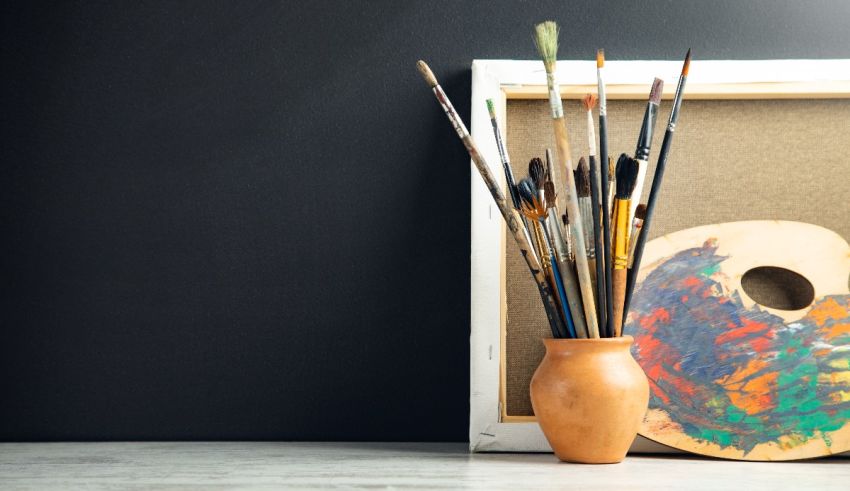 A vase filled with paint brushes and a palette on a table.