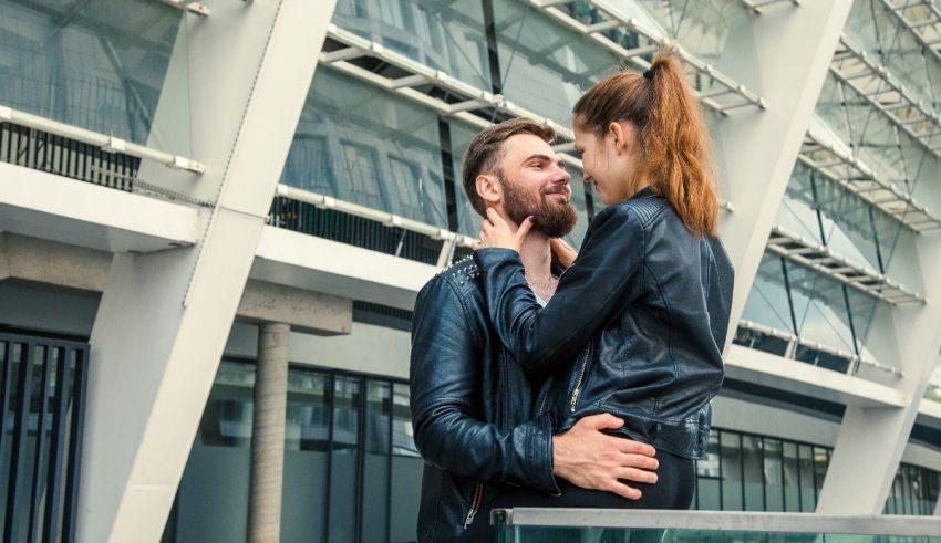 A man and woman kissing in front of a modern building.
