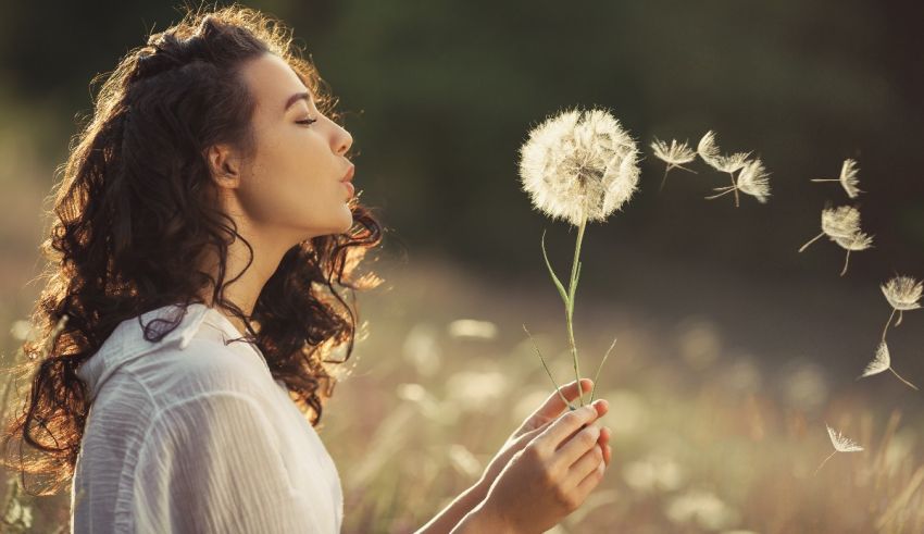 A woman blowing a dandelion in a field.
