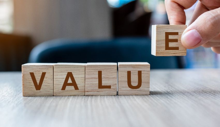 A person is holding wooden blocks that spell out the word value.