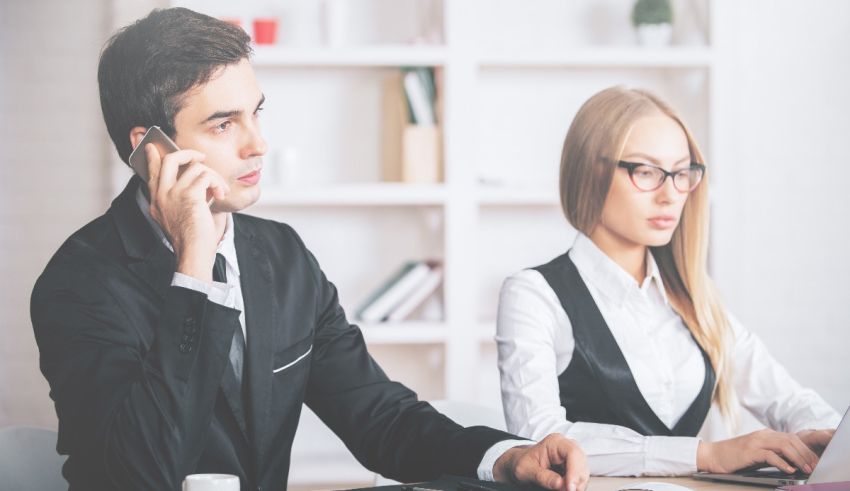 A man and woman talking on the phone while sitting at a desk.