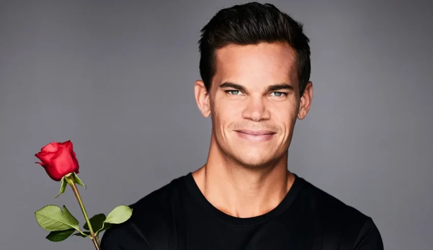 A man holding a rose in front of a gray background.