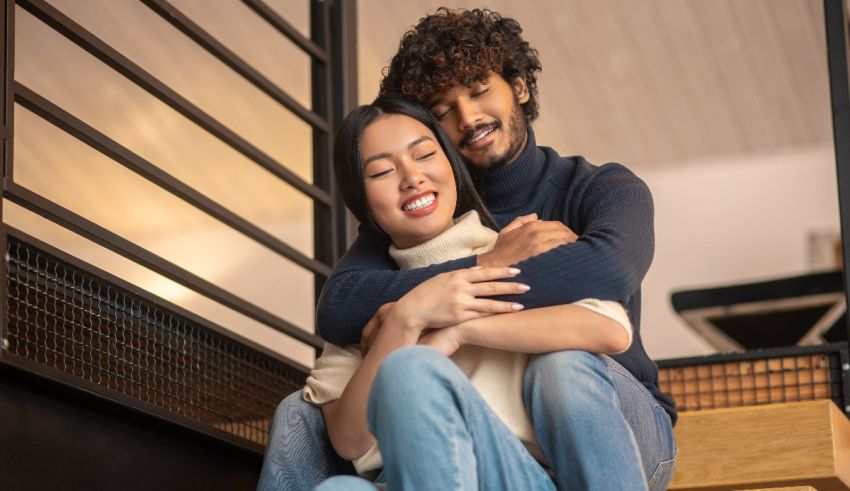 A young asian couple hugging each other while sitting on the stairs.