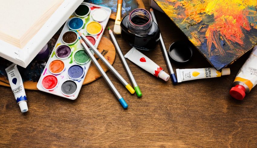 An artist's palette, paints and brushes on a wooden table.