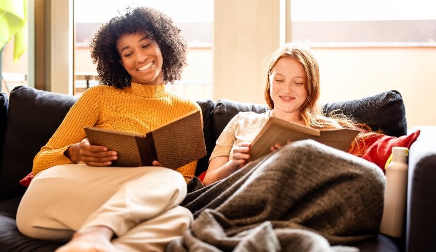 Two women sitting on a couch reading books.