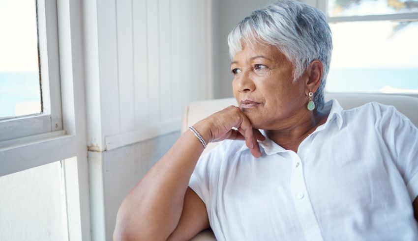 An older woman sitting in a chair looking out the window.