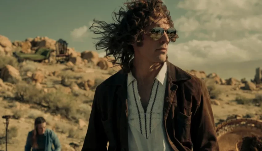 A man with long hair is standing in the desert.