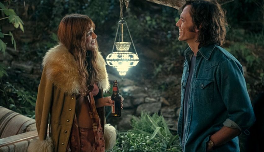 A man and woman standing next to a lantern in a wooded area.