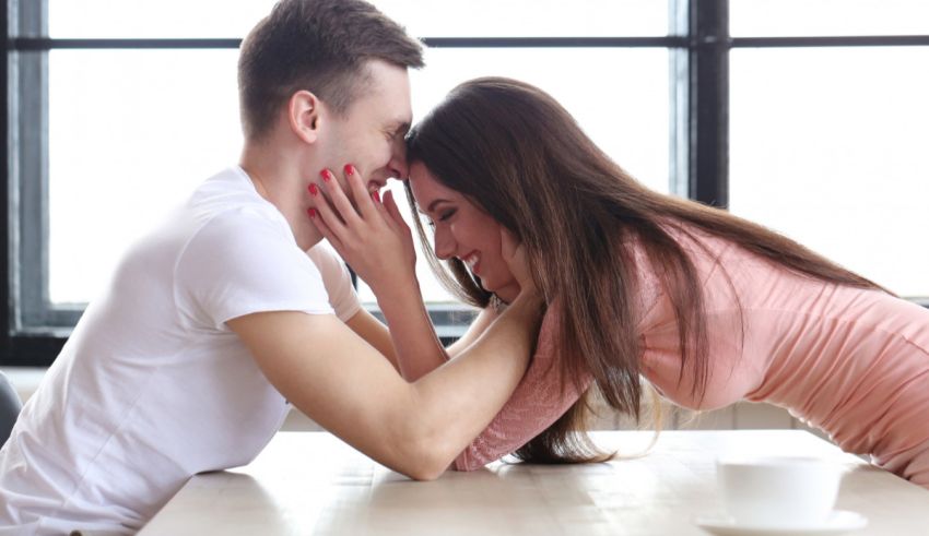 A man and a woman kissing at a table.
