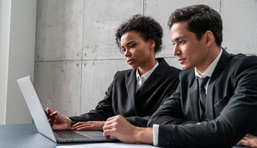 Two business people sitting at a table looking at a laptop.