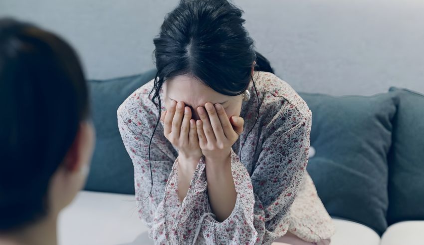 A woman is covering her face while sitting on a couch.