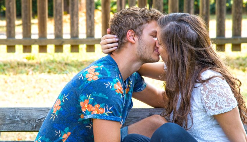A couple kissing on a bench in a park.