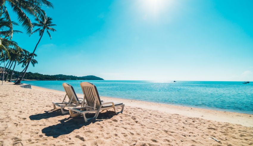 Two lounge chairs on a sandy beach in thailand.