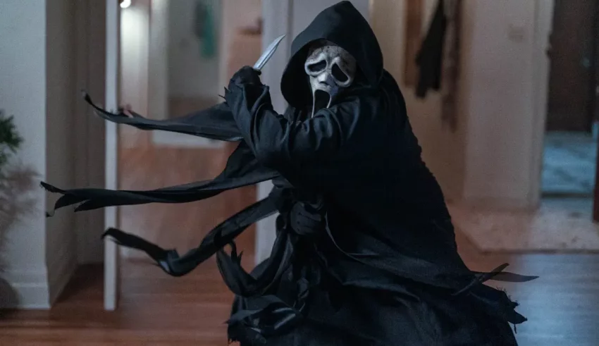 A man in a black hooded robe is standing in a hallway.
