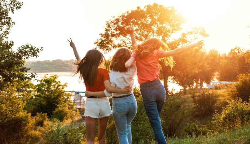 Three friends are standing on a hill with their arms raised in the air.