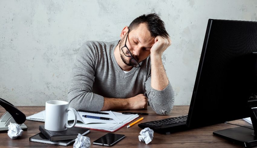 A man is sitting at his desk with his head resting on his head.