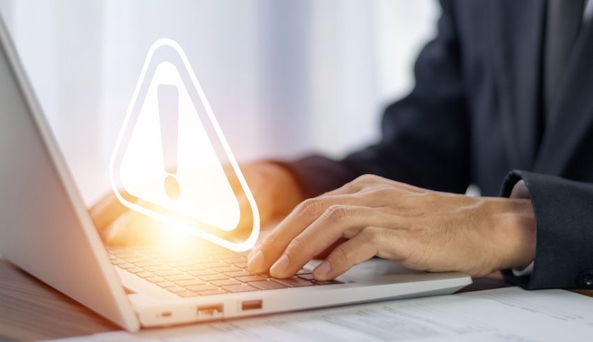 A man is typing on a laptop with an exclamation mark on it.