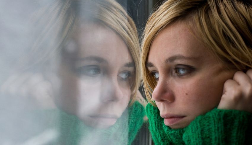 A woman in a green sweater looking out of a window.