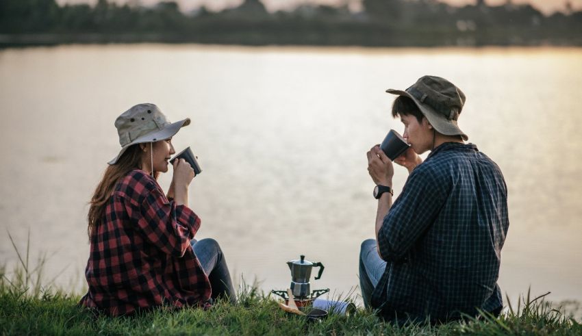 Two people sitting on the grass near a lake.