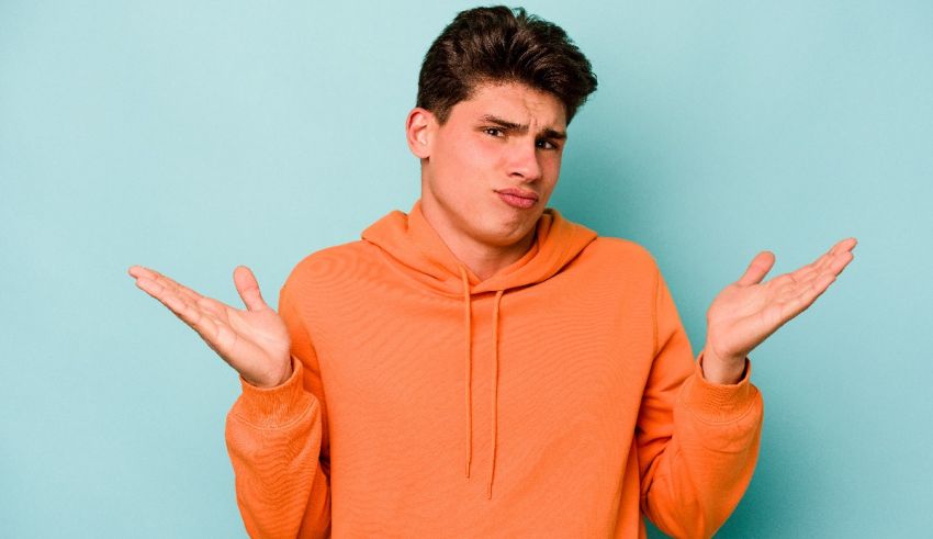 A young man in an orange sweatshirt making a confused gesture.