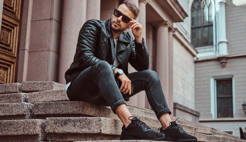 A man wearing a black leather jacket and sunglasses sitting on steps.