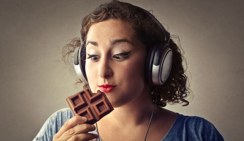 A woman with headphones eating a chocolate bar.