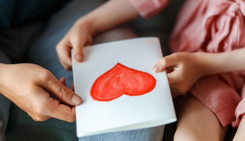 A child is holding a red heart on a piece of paper.