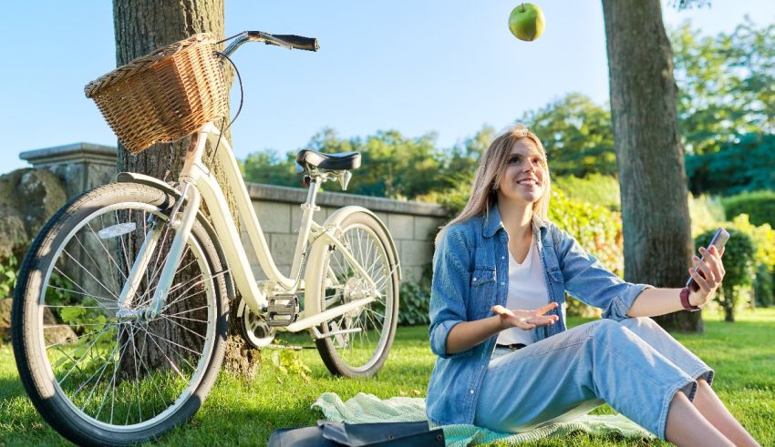 A woman sitting on the grass with a bicycle and an apple.