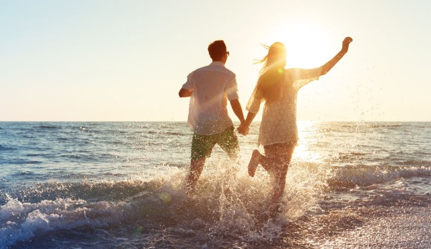 Two people running in the ocean at sunset.