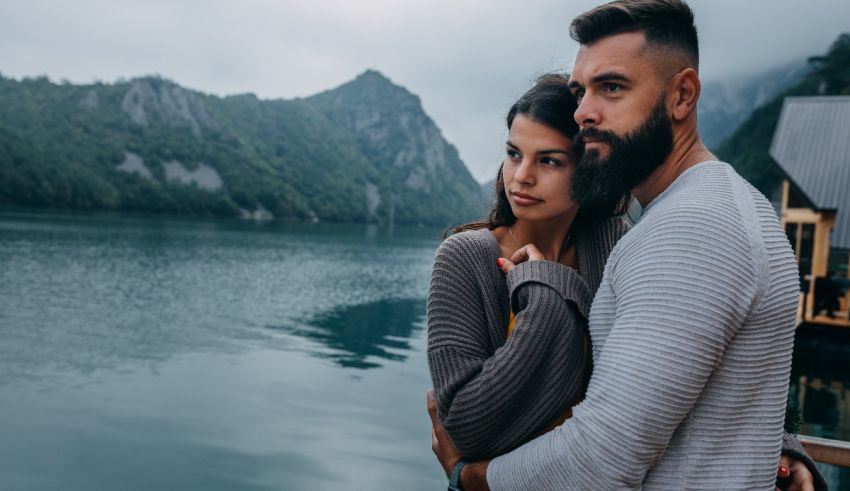 A man and woman standing next to a lake with a bearded man.