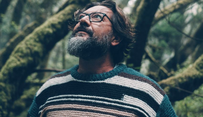 A bearded man in a striped sweater standing in a forest.