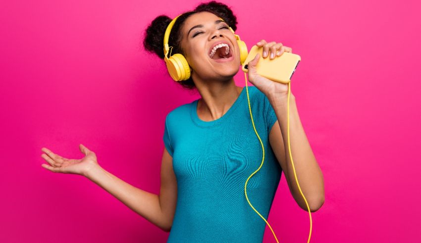 A young woman singing into a microphone against a pink background.