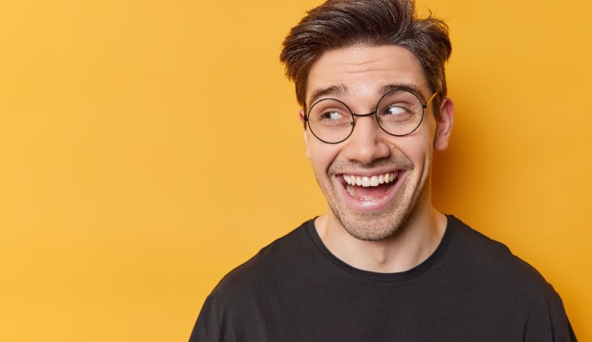 A man in glasses is laughing against a yellow background.