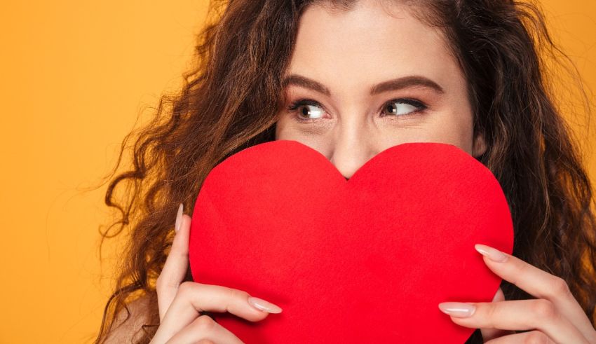 A young woman is holding a red heart over her face.