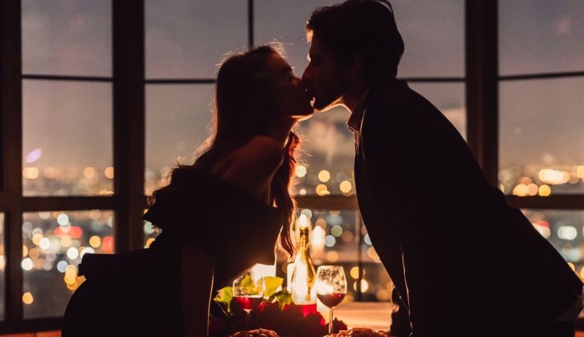 A couple kissing in front of a window at night.